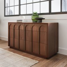 a large wooden cabinet sitting in front of a window next to a rug and vase