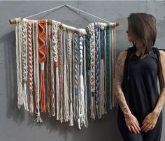 a woman standing next to a wall covered in different colored ropes and chains hanging from it's sides