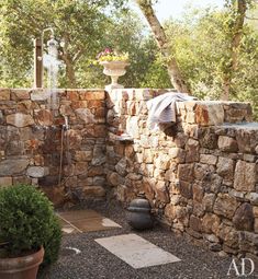 an outdoor shower in the middle of a stone walled area with potted plants on either side