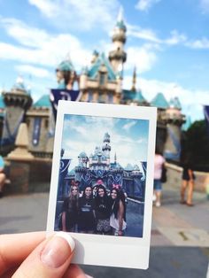 a person holding up a polaroid photo in front of a castle at disney world