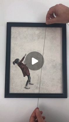 a person holding up a framed photo with a stick in front of it that has a drawing of a man swinging a tennis racquet