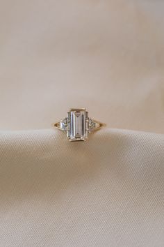 an emerald cut diamond ring sitting on top of a white cloth