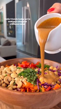 a person pouring dressing into a bowl filled with vegetables, beans and other things in it