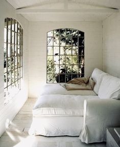 two white couches sitting next to each other in a room with windows on the wall