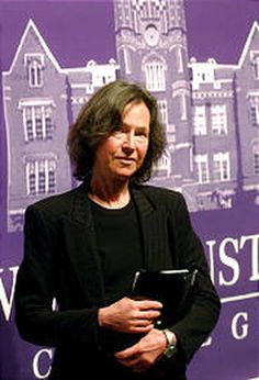 a woman standing in front of a purple backdrop holding a book and looking at the camera