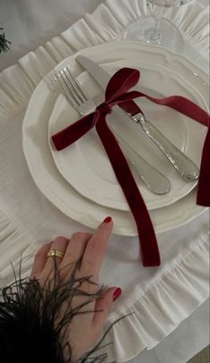 a woman's hand on a white plate with red ribbon and silverware in front of her