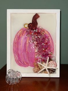 a pink pumpkin with seashells and starfish on it in a white frame