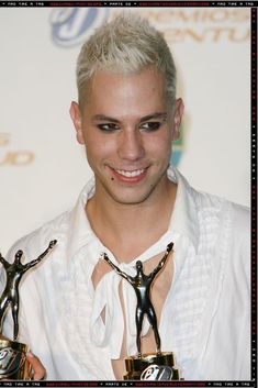 a man with blonde hair holding two awards in his hands and smiling at the camera