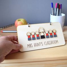 a person is holding a wooden sign that says, mrs hunt's classroom with pencils and an apple in the background