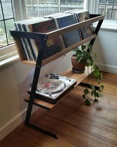 a record player is sitting on a shelf in front of a window with books and plants