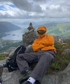 a man in an orange jacket sitting on top of a rock next to a backpack