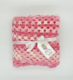 a pink and white crocheted blanket with a tag on it's side