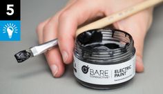 a person holding a paint brush near a jar of black acrylic on a table