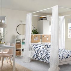 a white canopy bed sitting in a bedroom next to a dining room table and chairs