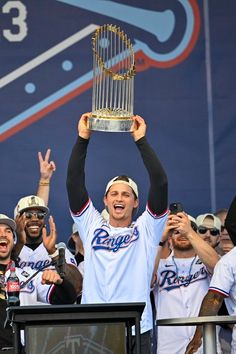 a baseball player holding up a trophy in front of his head while other players look on