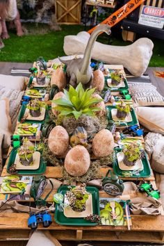 a long table with plates and plants on it in front of a dinosaur head planter