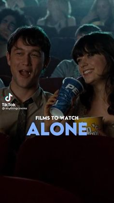 two people sitting in a movie theater and one is holding a cup while the other looks on