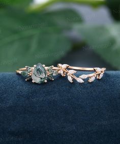 a close up view of a ring with leaves and stones on the side, sitting on top of a blue velvet surface