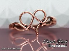 a rose gold ring with two intertwined hearts on it's sides, sitting on a pink surface