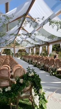 an outdoor wedding venue set up with white drapes and greenery on the ceiling