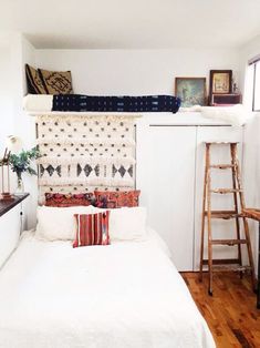 a white bed sitting in a bedroom next to a wooden ladder and window sill