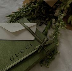 an envelope is tied with a ribbon and sitting on top of a green book next to flowers