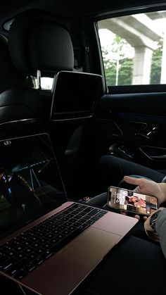 a laptop computer sitting on top of a car seat next to a person holding a cell phone