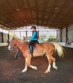 a woman riding on the back of a brown horse in an indoor arena next to another person