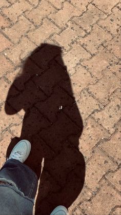 the shadow of a person's legs and shoes on a brick sidewalk with a blue shoe