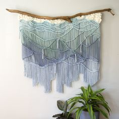 a wall hanging made out of yarn and wood sticks next to a potted plant