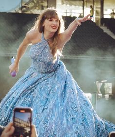 a woman in a blue dress is holding her cell phone