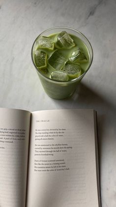 an open book sitting on top of a table next to a cup filled with ice cubes