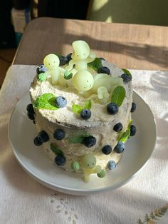 a white plate topped with a cake covered in frosting and blueberries on top of a table