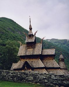 an old wooden church with thatched roof and steeple in front of a mountain