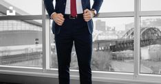 a man wearing a suit and tie standing in front of a window with a view of a bridge