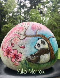 a painted rock with a panda bear and cherry blossom tree on it's face