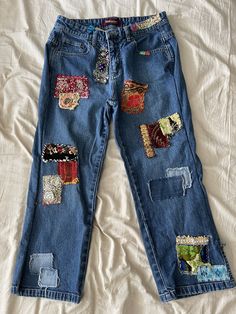 a pair of blue jeans with patches and sequins on them sitting on a bed
