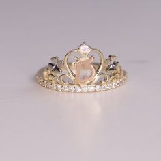 a gold and diamond ring with the letter e on it's side, sitting on a white surface