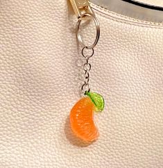 an orange keychain hanging from a white purse with a green leaf on it