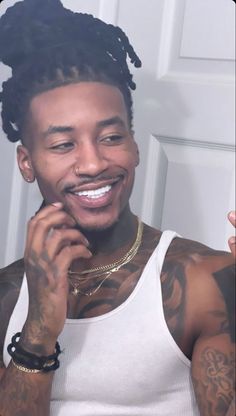 a man with dreadlocks and tattoos on his face smiles at the camera while wearing a white tank top