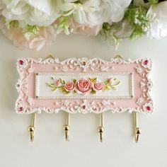 there is a pink and white wall hanging with flowers on it next to some hooks