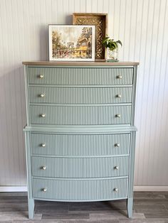 a blue dresser with gold knobs in a room next to a painting on the wall