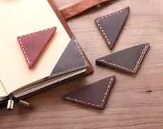 three triangle shaped leather coasters sitting on top of a wooden table next to an open notebook