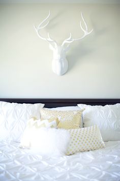 a white deer head mounted on the wall above a bed with pillows and throw pillows