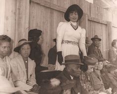 an old black and white photo of a woman standing in front of a group of people