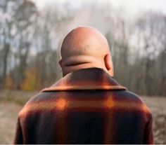 the back of a man's head as he stands in front of a wooded area