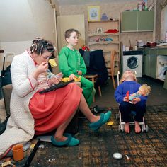 two women and a child sitting on the floor in a room with other people around