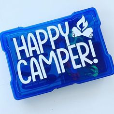 a blue happy camper lunch box sitting on top of a white table with the words happy camper printed on it