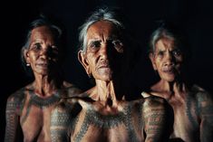 three older women with tattoos on their body and chest, standing in front of a dark background