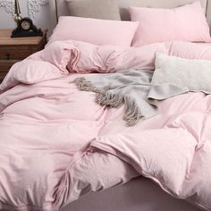 a bed with pink comforter and pillows on top of it, next to a night stand